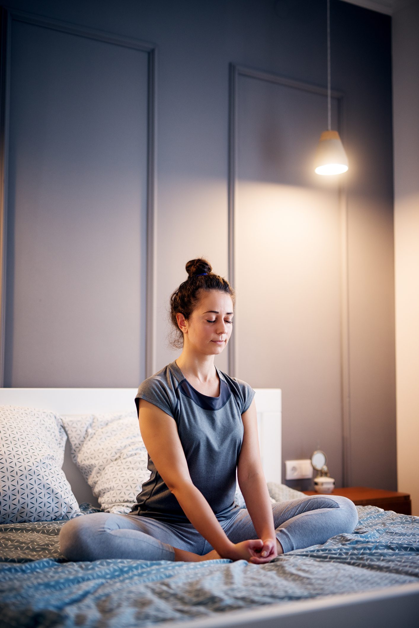 Peaceful pretty middle aged active woman practising yoga on the bed holding eyes closed